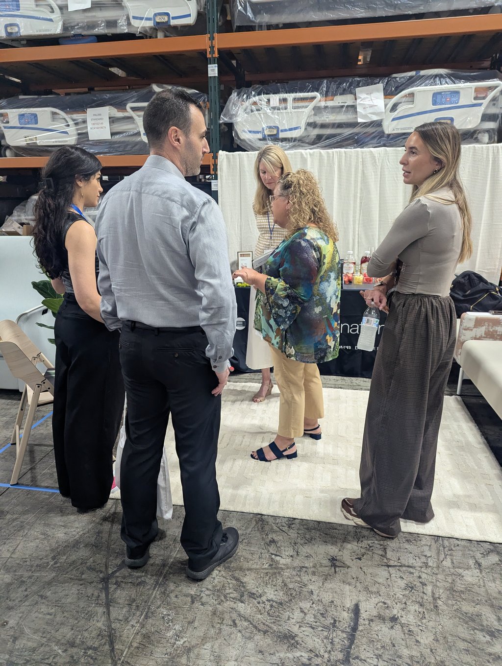 Five attendees in conversation in a warehouse aisle in front of shelves of wrapped hospital beds