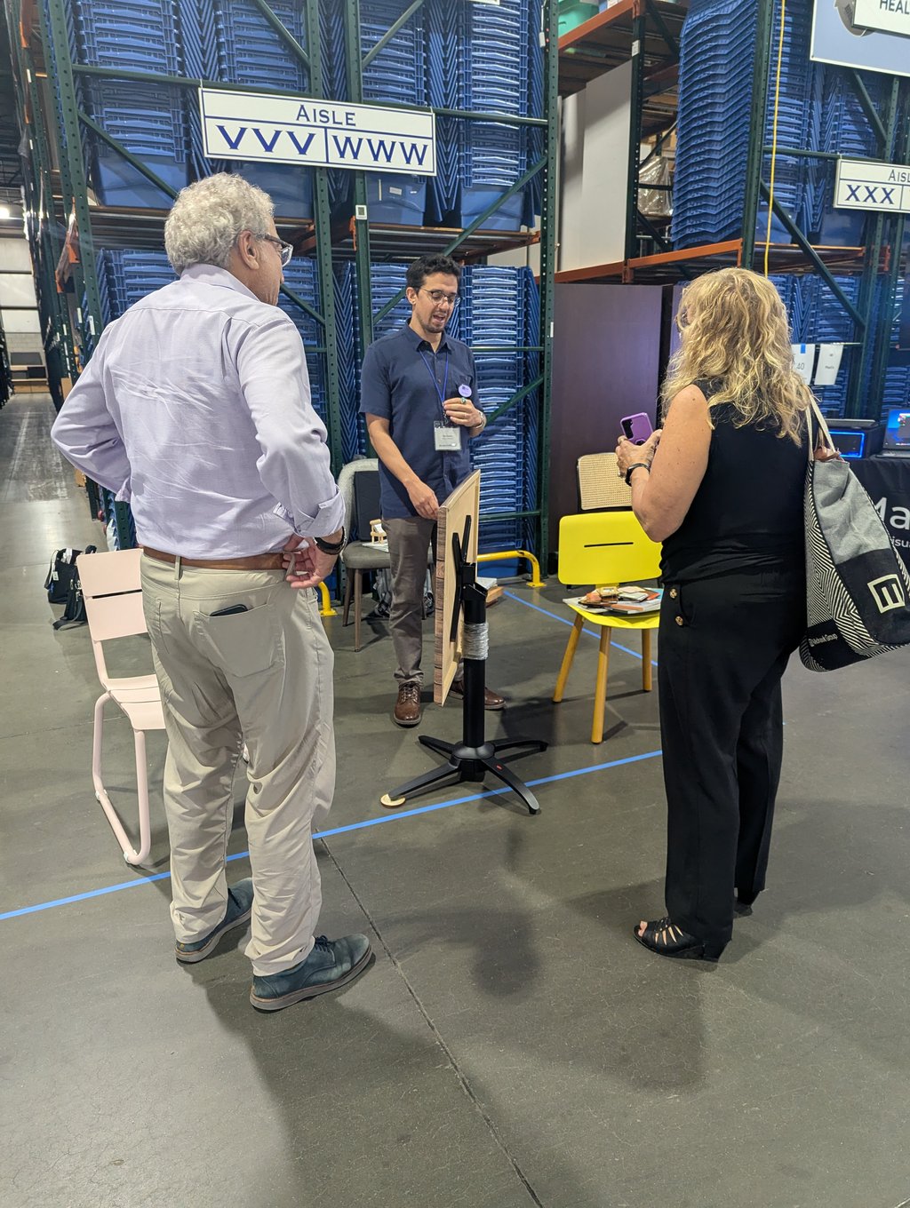 Three attendees talking among chairs and display items in an aisle of blue bin racking