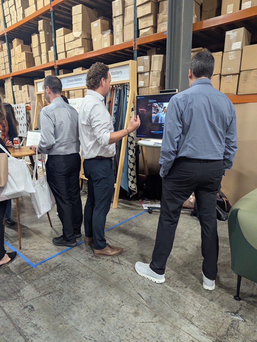 Three attendees at a fabric sample display and monitor below the Choice Matters sign