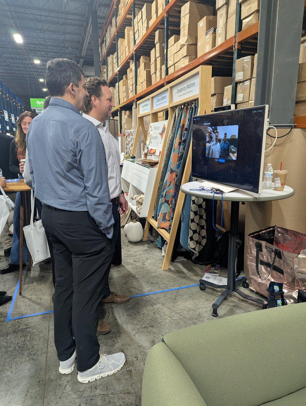 Two attendees watching a monitor beside the fabric samples under the Choice and Creativity Matters signs