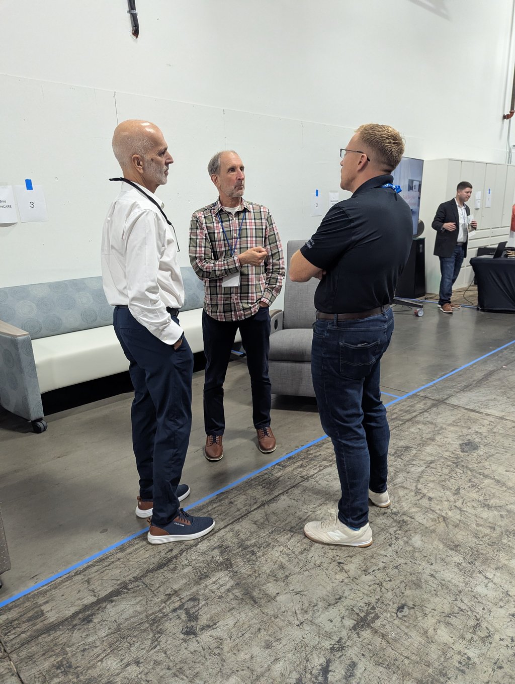 Three attendees talking in an industrial room with the numbered booth signs 2 and 3 on the wall behind