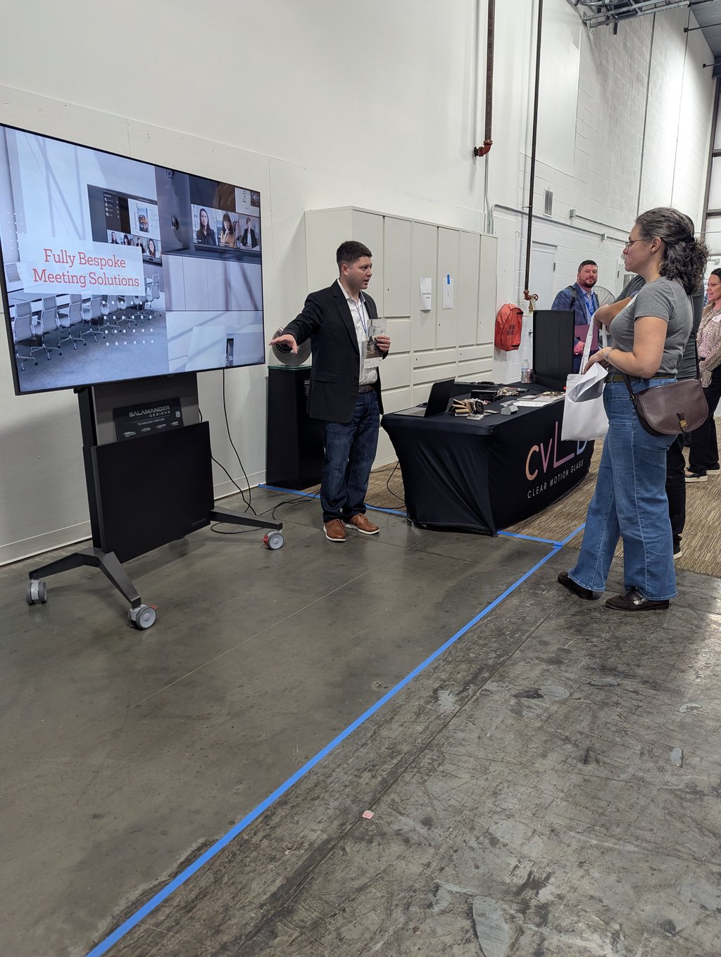 A presenter talking to attendees beside a screen reading Fully Bespoke Meeting Solutions at the Salamander stand
