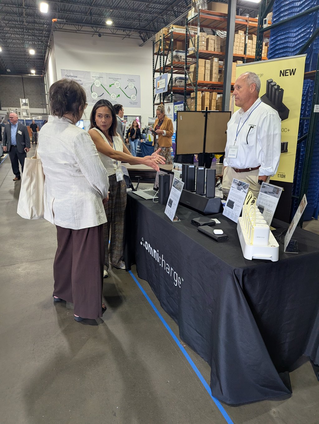 Three attendees talking at the Omnicharge table with charging units and a docking station on display