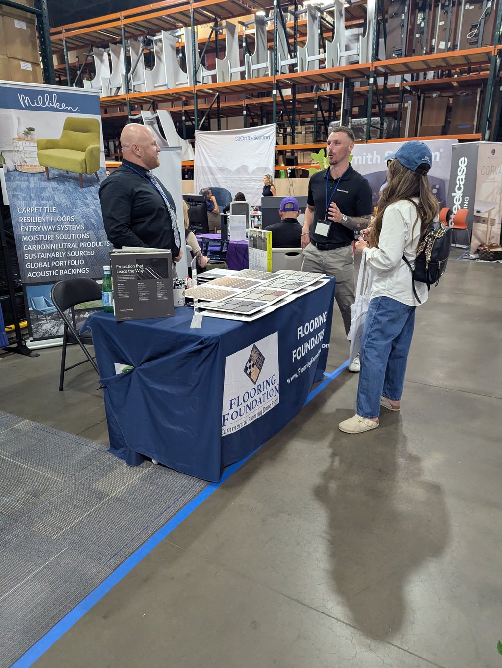 Three attendees at a table of flooring swatches and brochures below the Milliken and Flooring Foundation banners