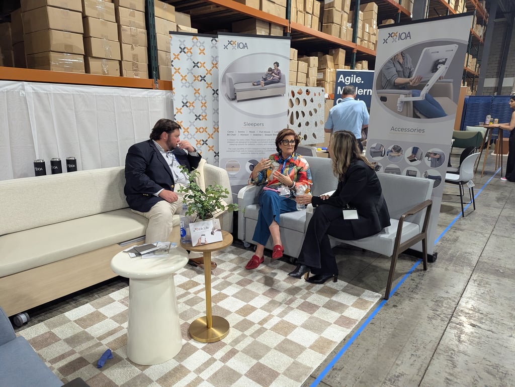 Three attendees seated on showroom sofas beneath the IOA banners for sleepers and accessories
