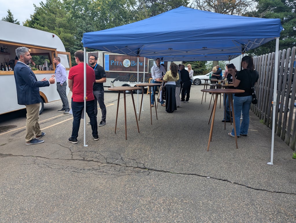 Attendees at tall cocktail tables under a blue canopy beside the Pita Bowl food truck
