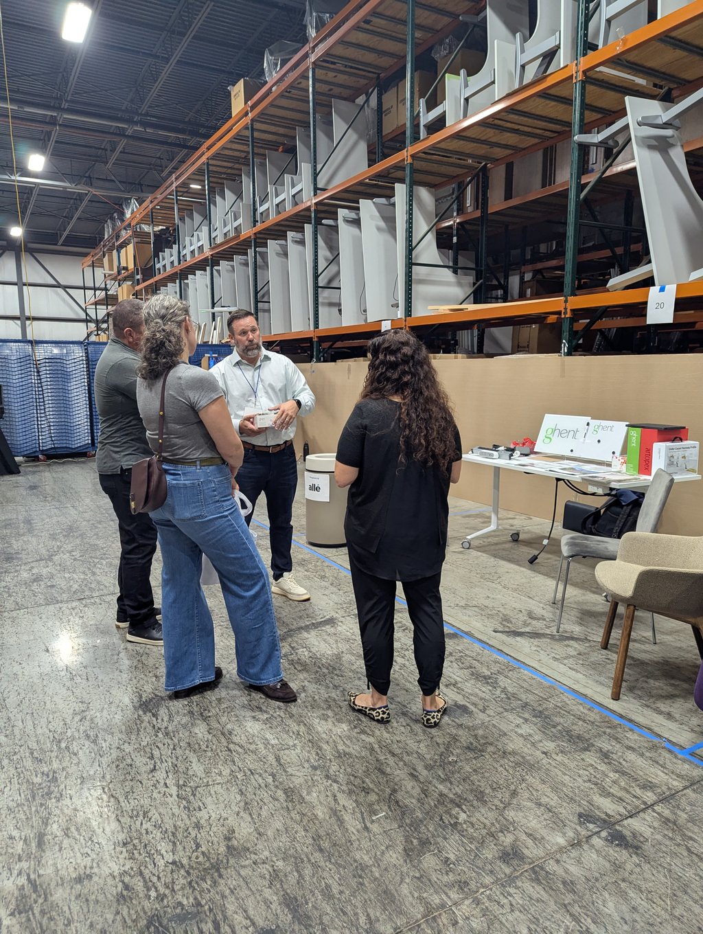 Four attendees talking at the Ghent display table in front of tall orange shelving