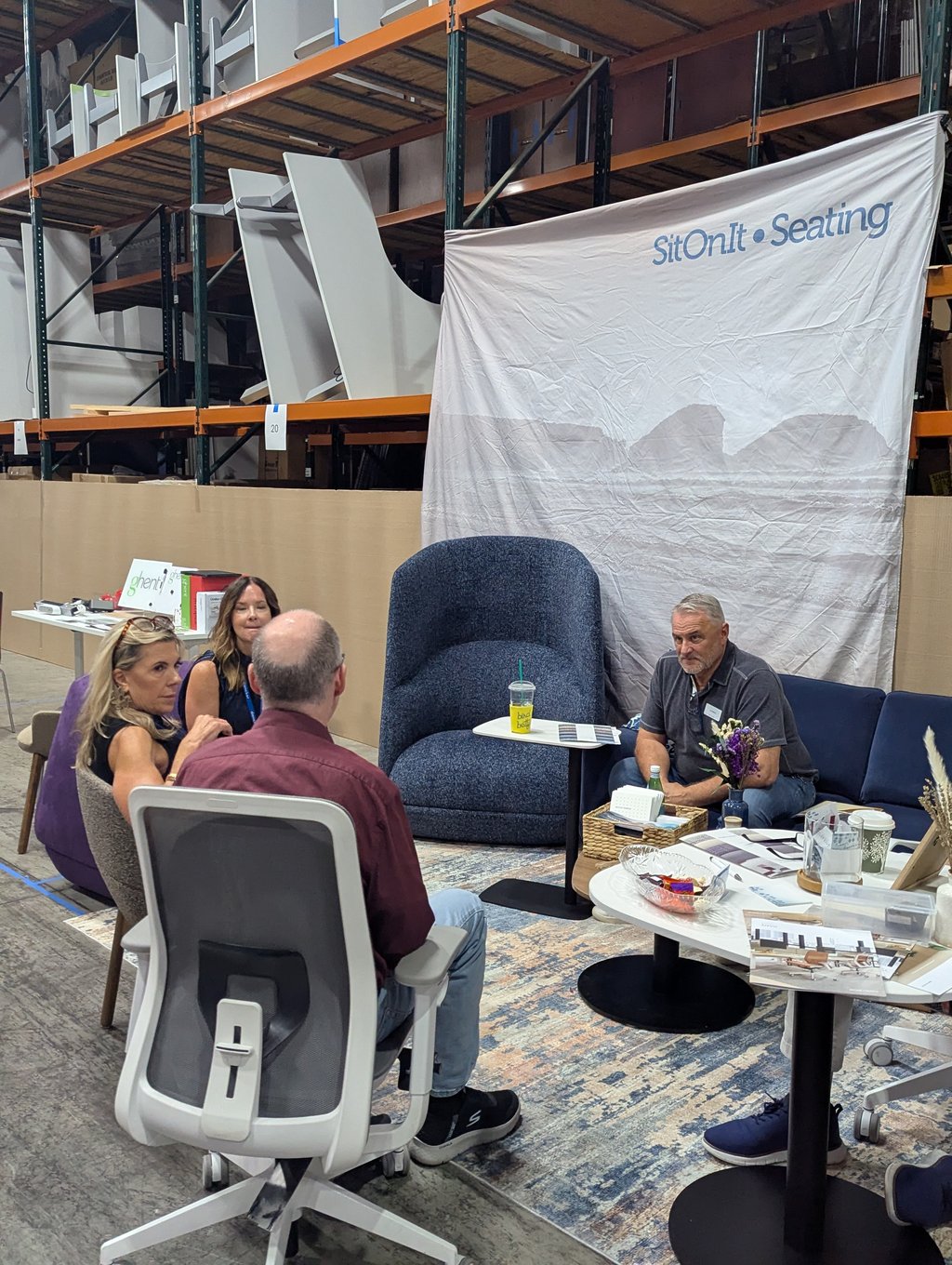 Attendees seated among sample office chairs and tables below the SitOnIt Seating banner