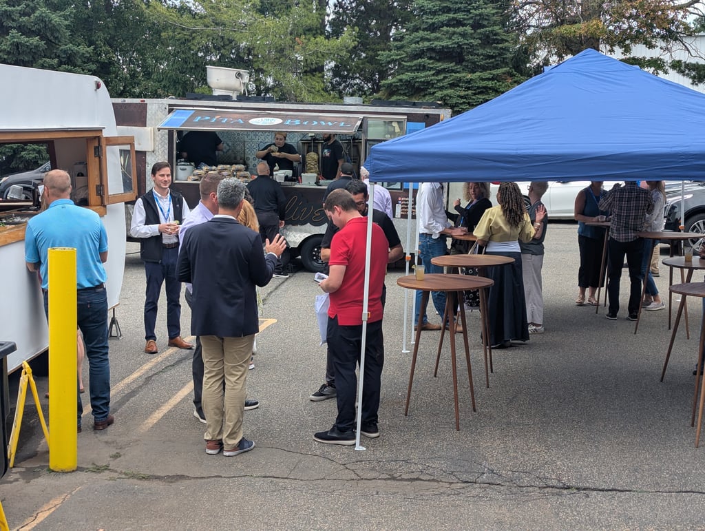 Attendees chatting under the blue canopy while staff prepare food at the Pita Bowl truck window
