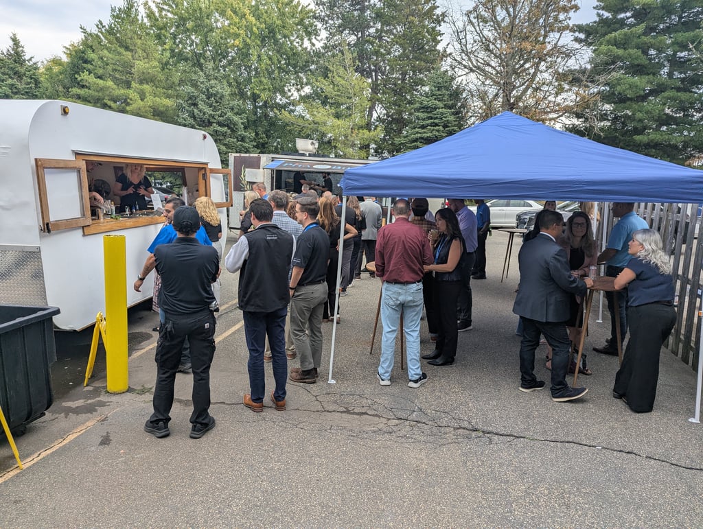 Attendees queuing at two food trucks with others eating under a blue canopy among the trees