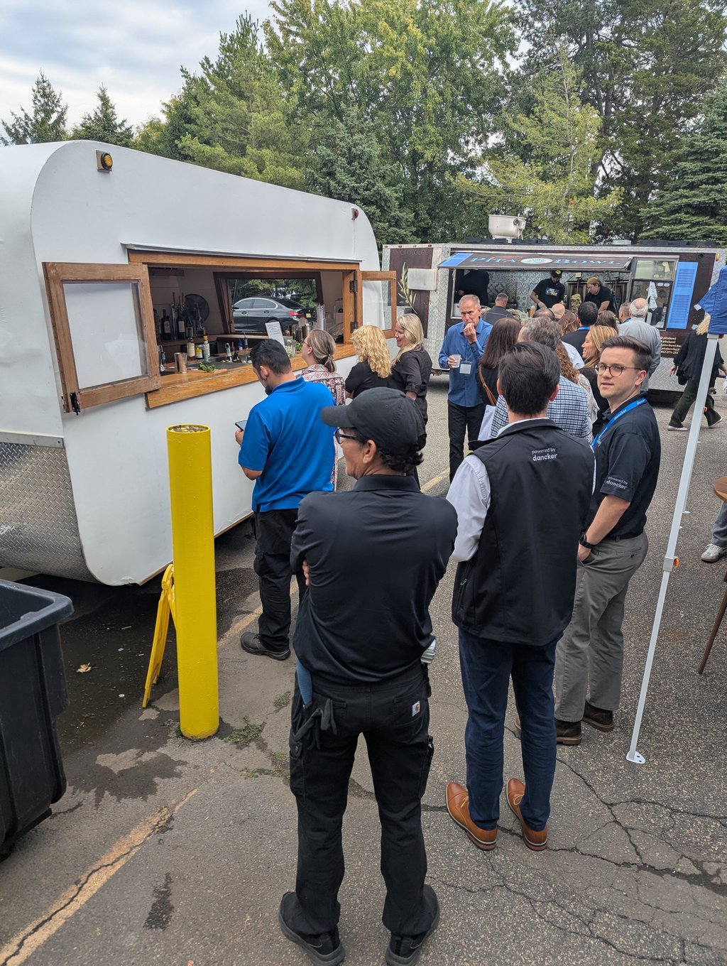 A crowd of attendees queuing at the food truck windows under the trees