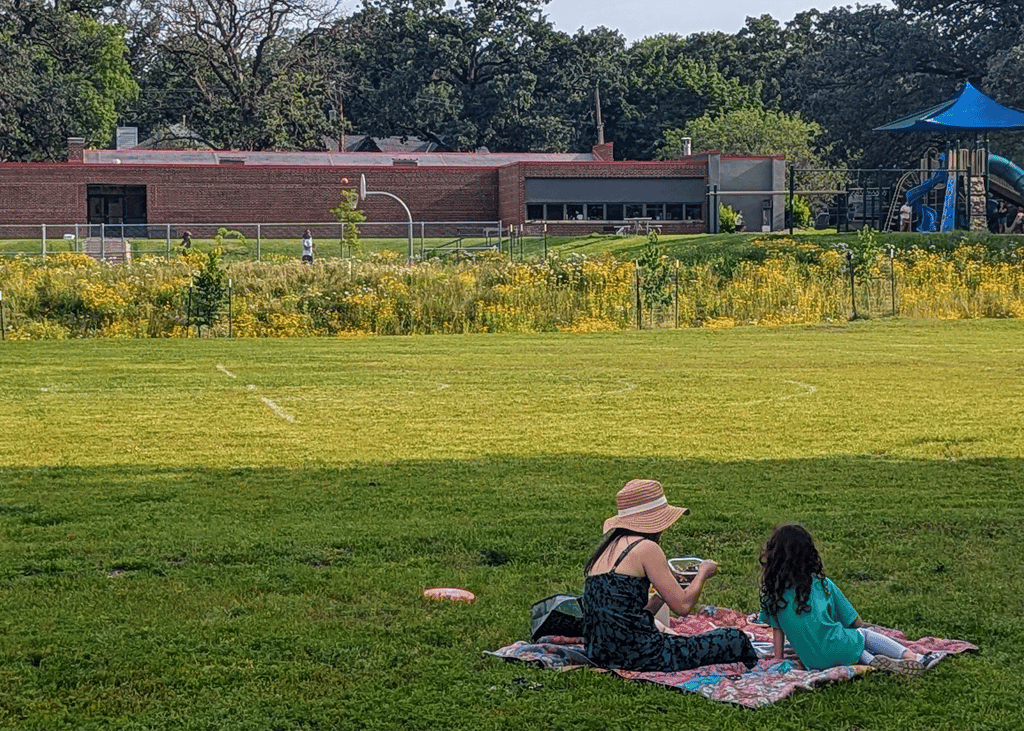 An adult and child sitting on a picnic blanket on the park lawn