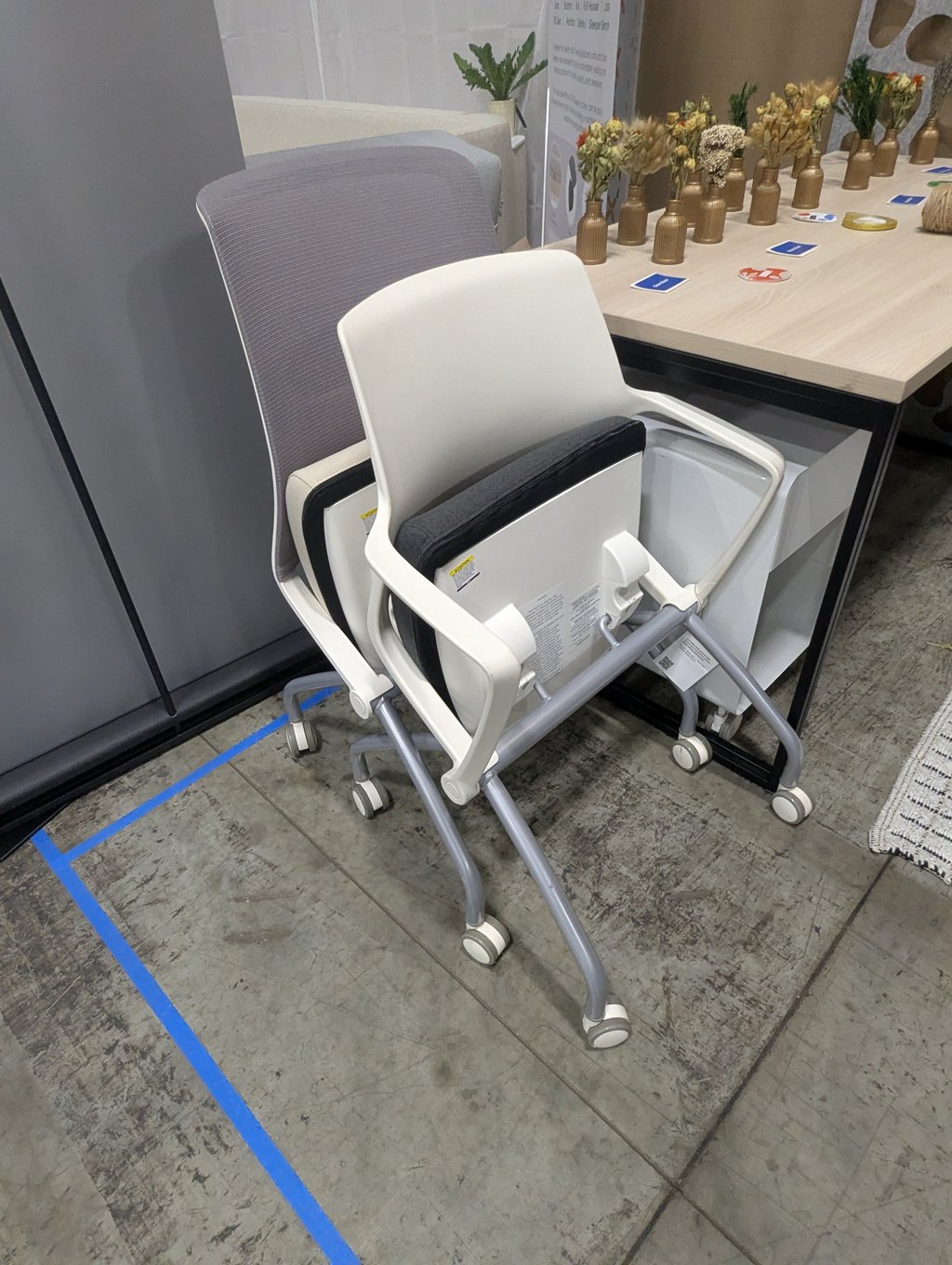 Office chairs nested on a wheeled frame beside a table of gold flower vases