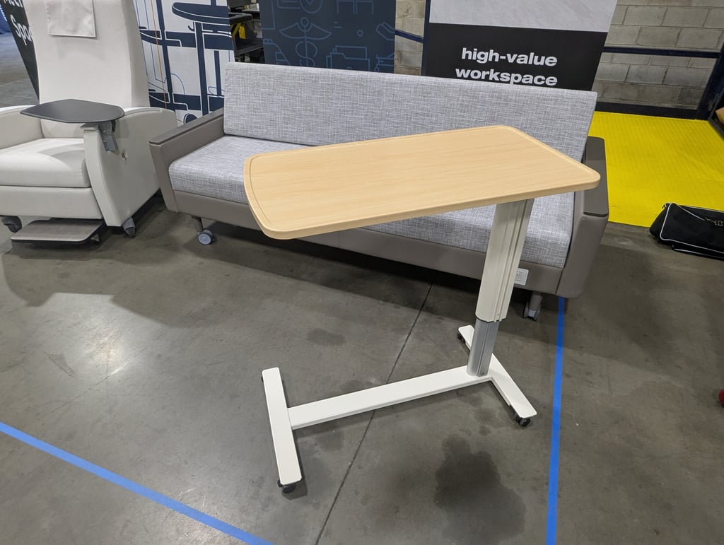 A height-adjustable overbed table in front of a bench and armchair