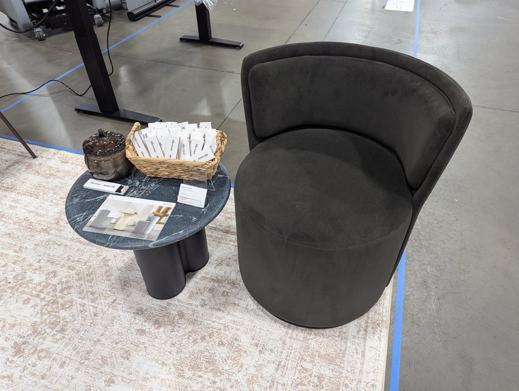 A dark grey upholstered Senator chair beside a marble-top side table of brochures