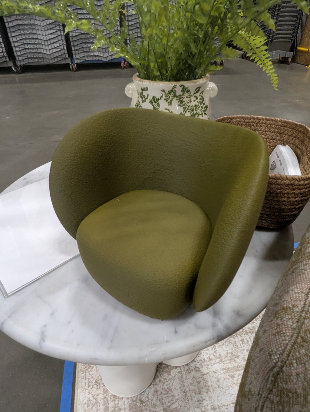 A green upholstered chair displayed on a round marble table beside a planted fern