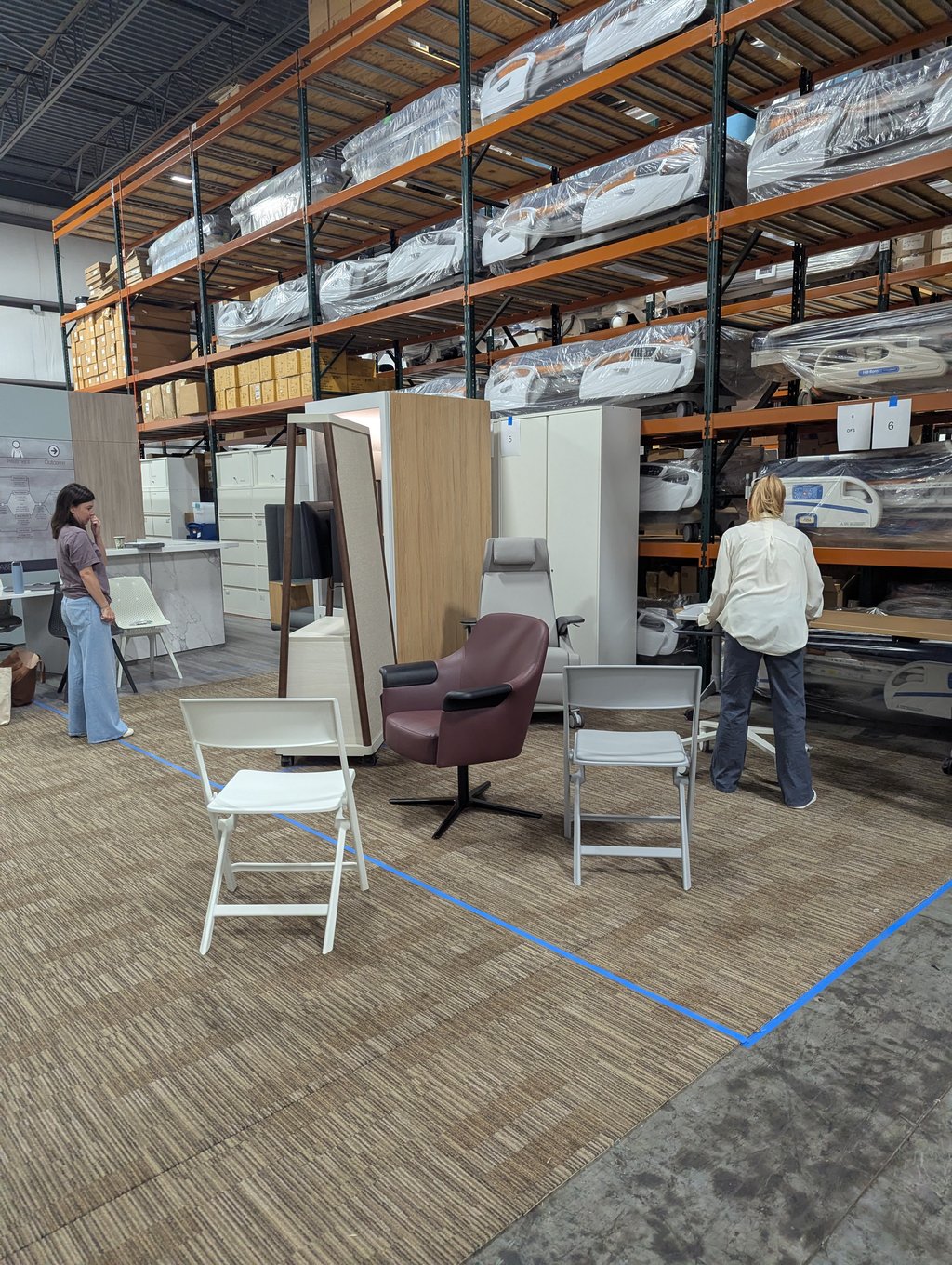 Seating staged on a taped-out carpet area beside racked hospital beds at booths 5 and 6