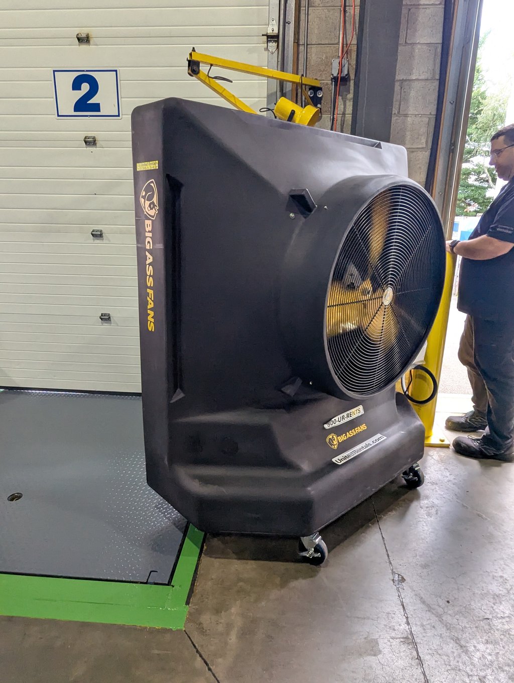 A large industrial fan on casters positioned by an open roll-up door