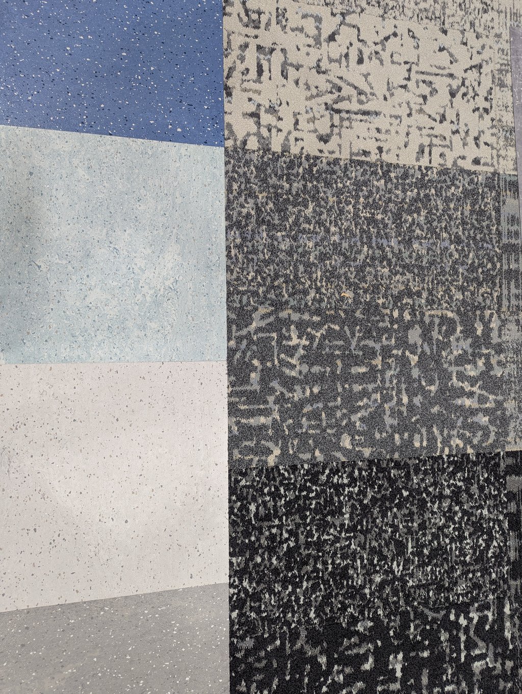 Close overhead detail where speckled vinyl tiles meet dark patterned carpet tiles