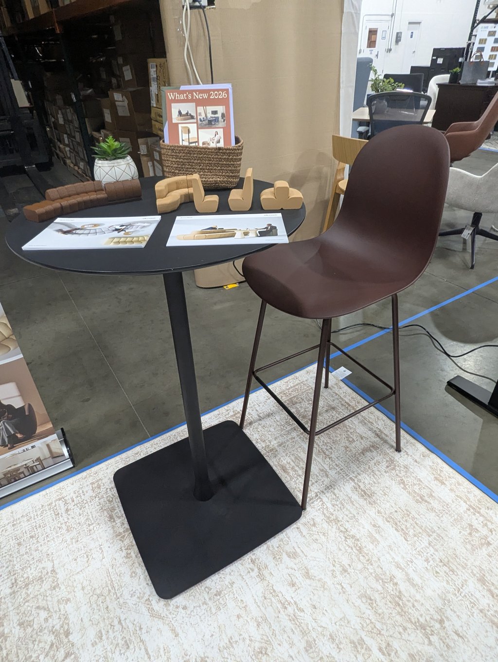 A What's New 2026 display table with seating models, brochures and a barstool