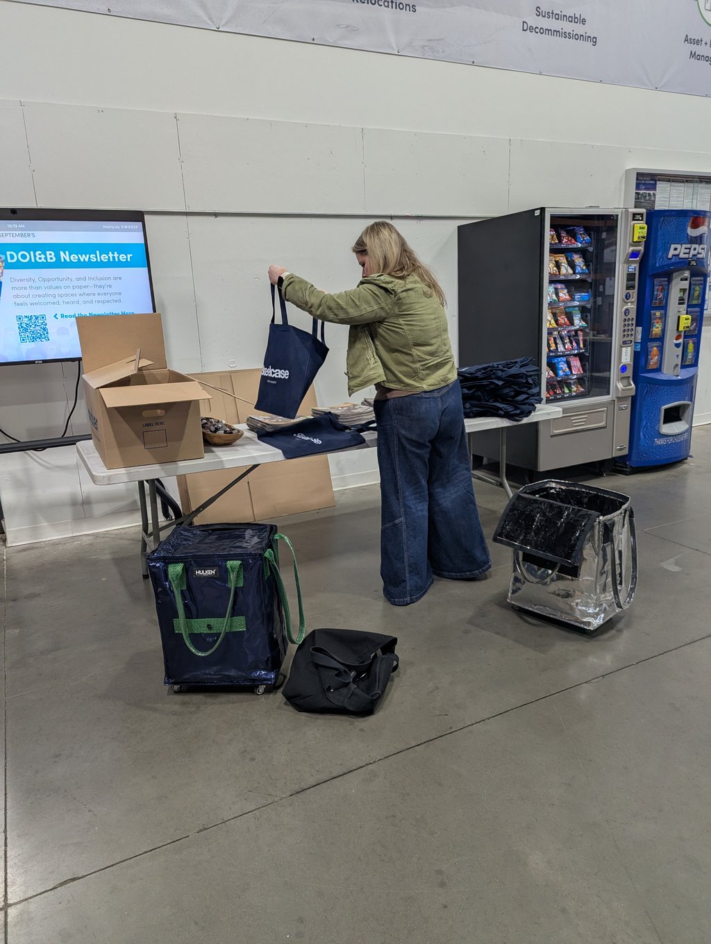 A team member filling navy Steelcase tote bags for attendees at a prep table