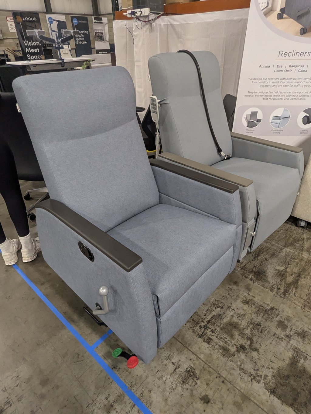 Two grey upholstered recliners on display, one with its hand control resting on the back
