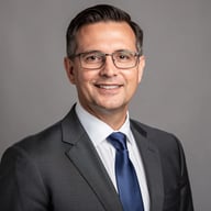 Professional headshot of a man in glasses and charcoal suit
