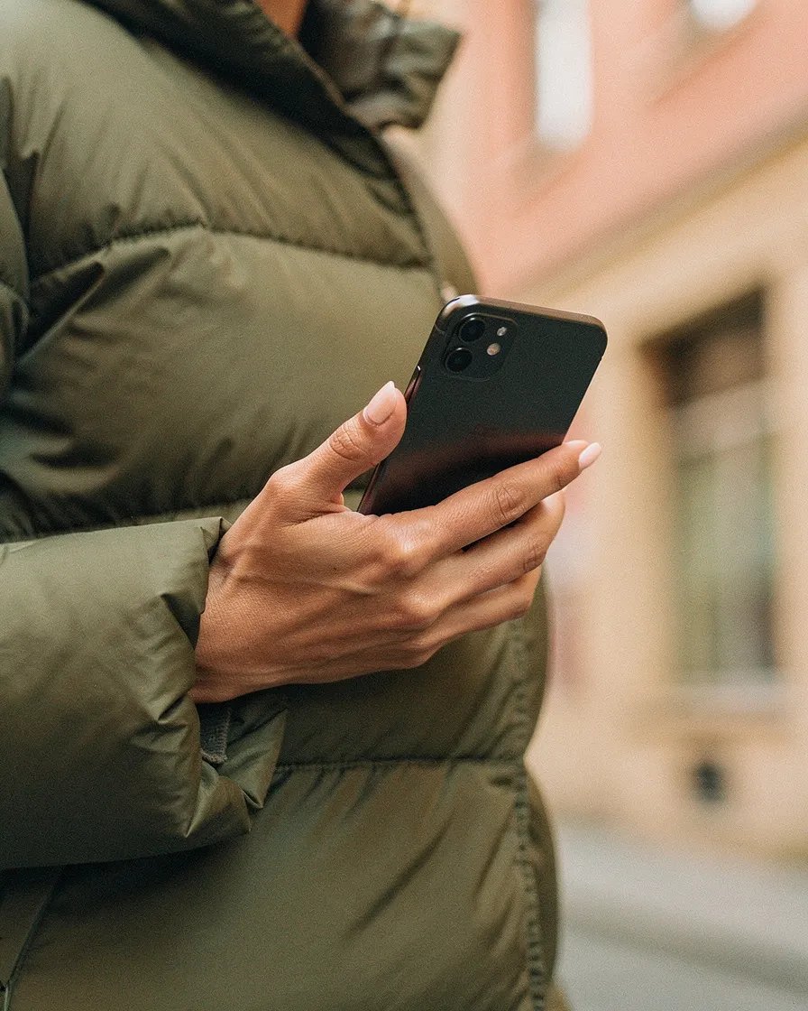 Woman's hand holding a smartphone in olive puffer jacket