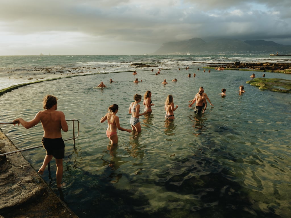 People swimming in a sheltered ocean pool against a rocky shoreline at golden hour