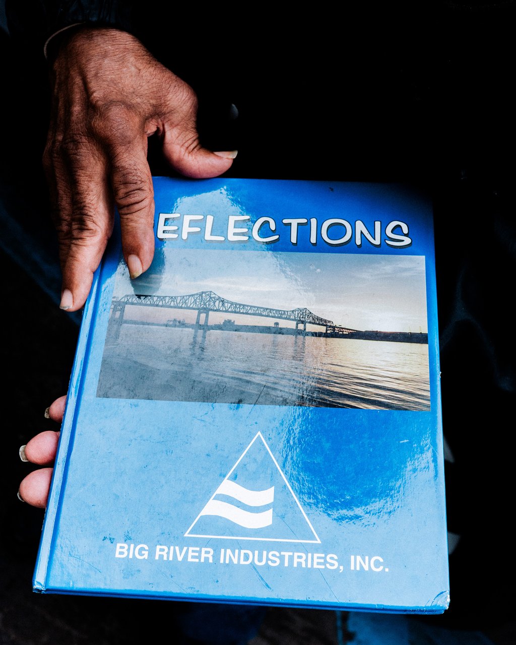 Close-up of a hand holding a blue brochure with a bridge photo and Big River Industries logo