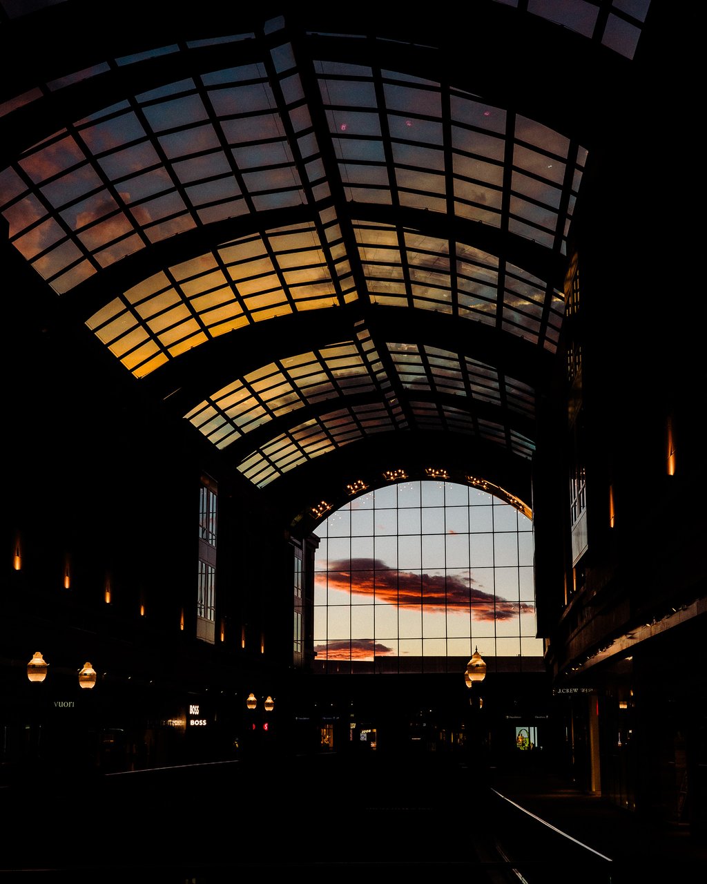 Silhouetted interior of a glass-roofed concourse with arched skylights framing a vivid sunset