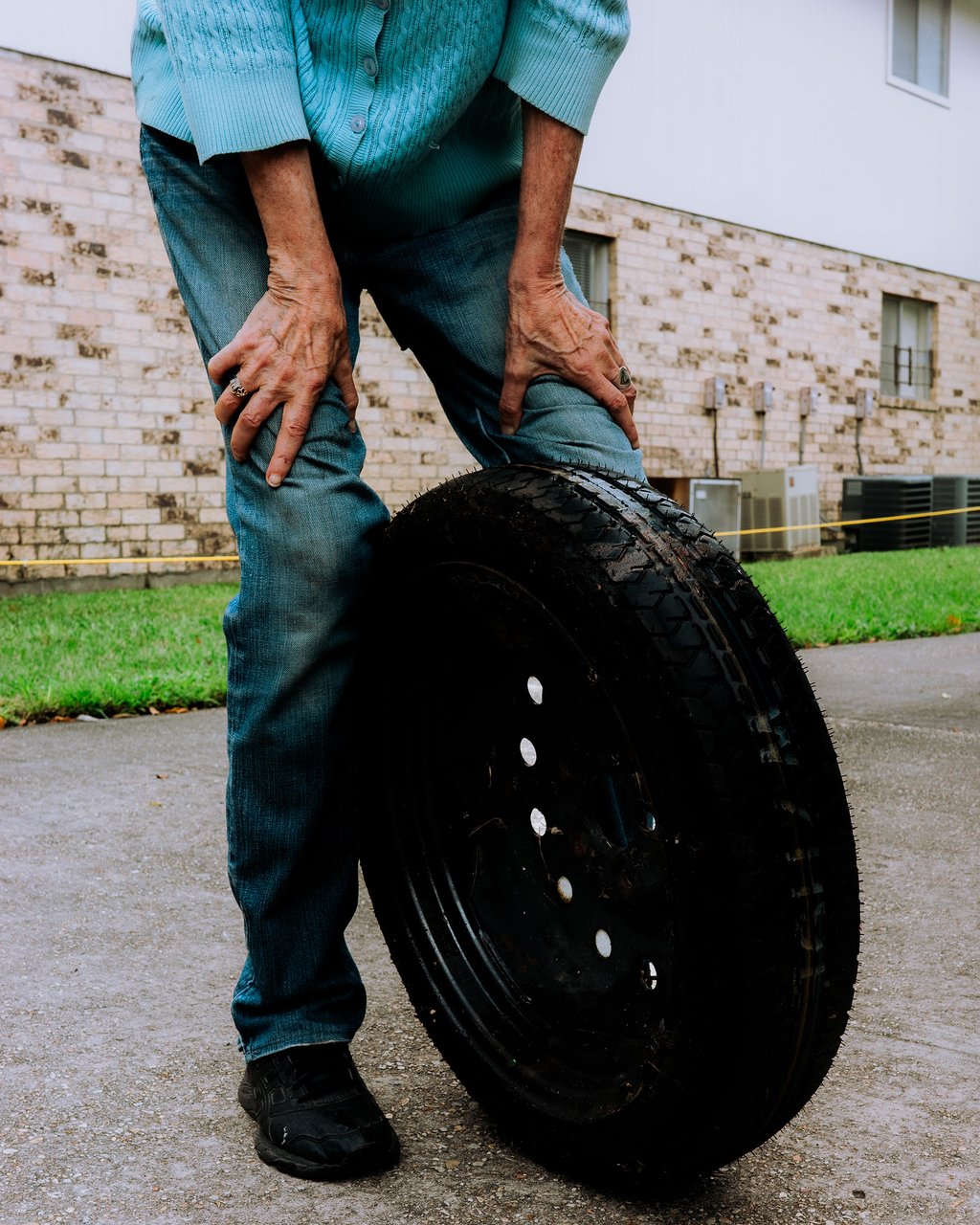 Close-up of a person in a blue sweater and jeans grasping a large black tire on wet pavement