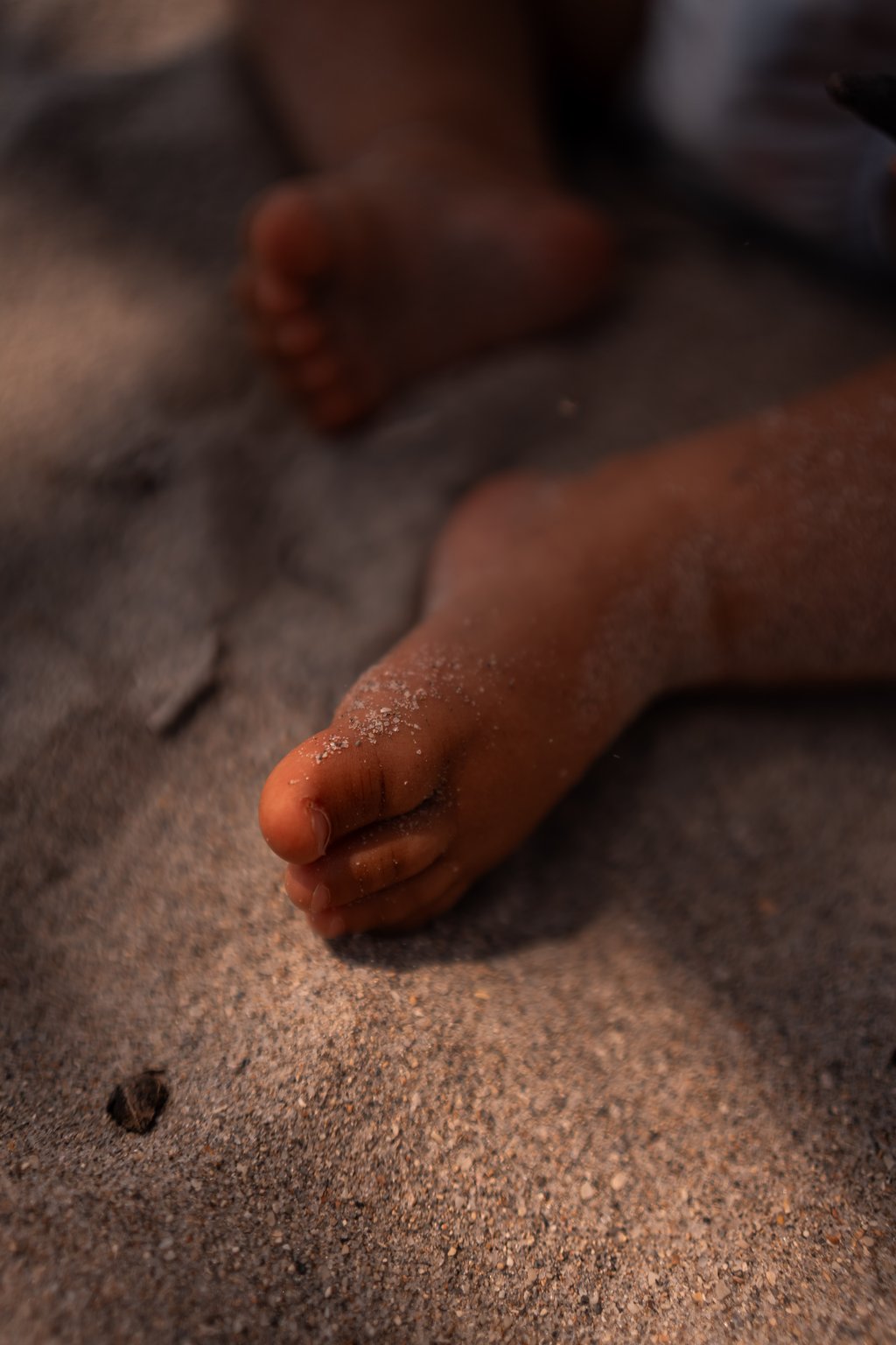 Close-up of bare feet resting on coarse sand with grains clinging to toes