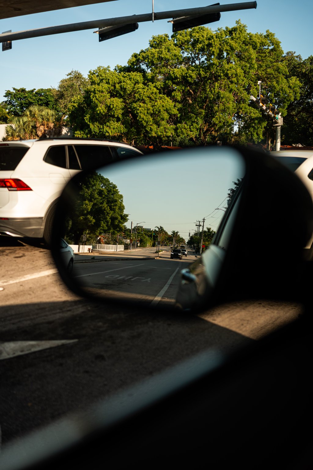 Street intersection seen from inside a car with a white SUV, traffic signal, and green trees ahead