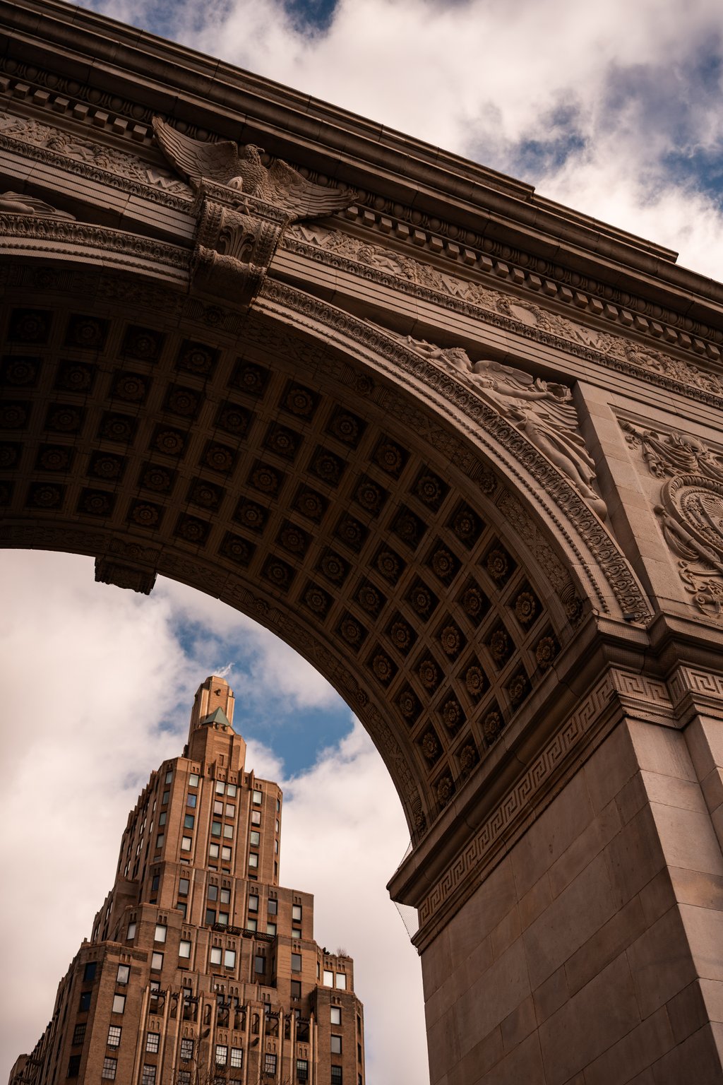 Monumental stone arch with carved eagle and coffered underside framing a tall brick skyscraper