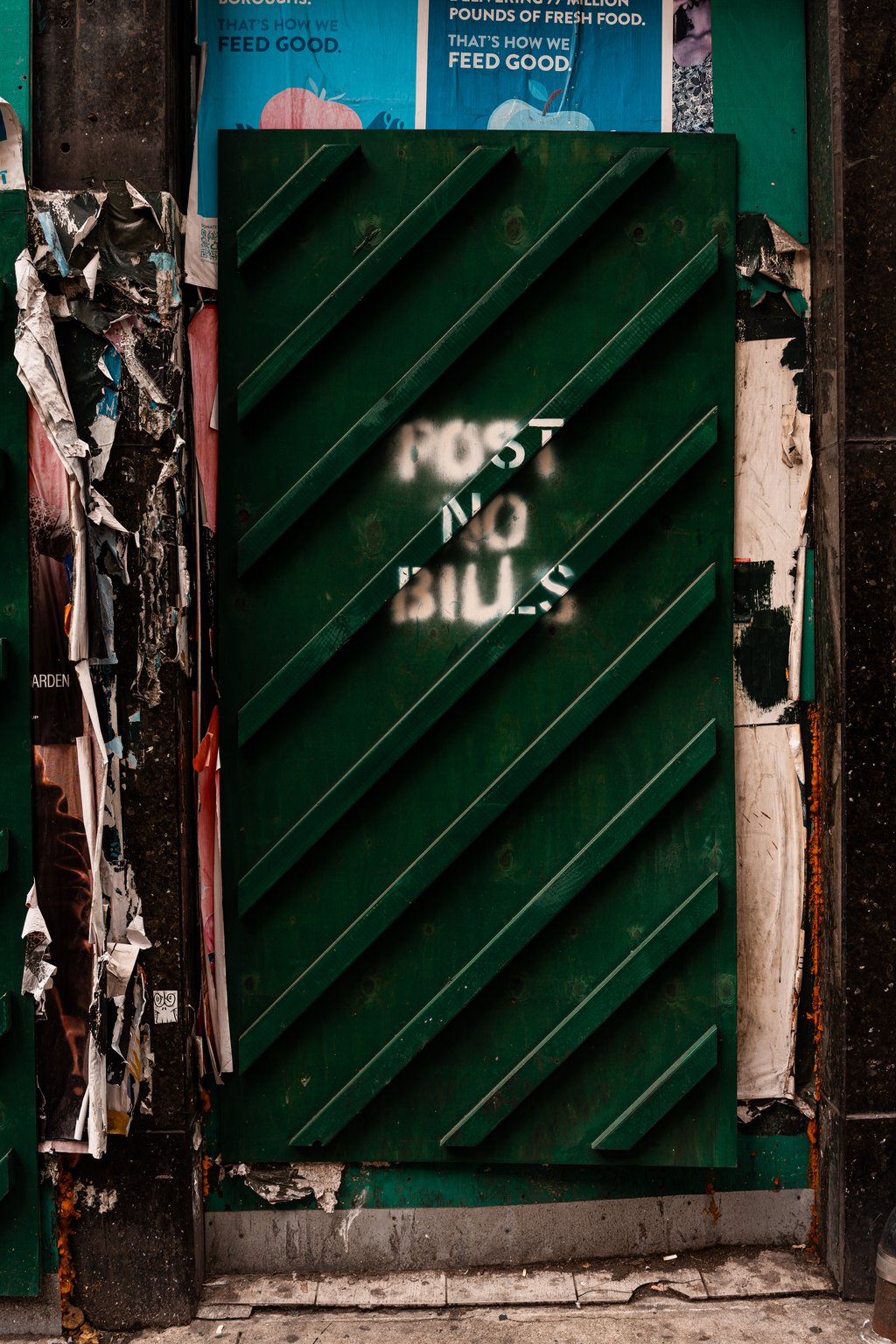 Weathered green boarded shutter with Post No Bills stencil and torn layered posters