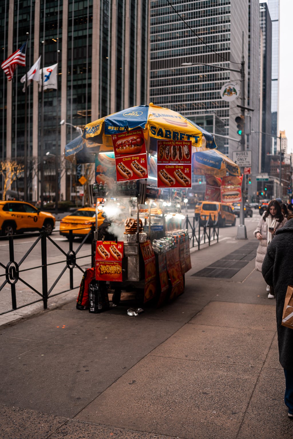 Busy city street with a Sabrett hot dog cart, yellow taxis, and tall buildings in the background