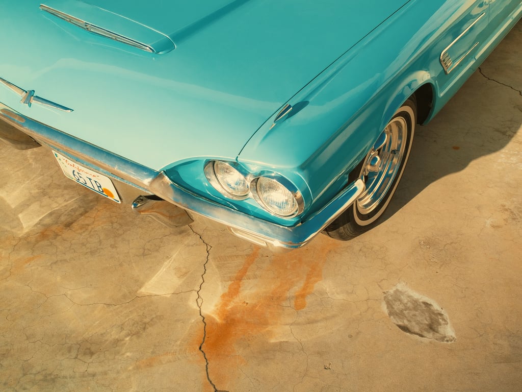 Close-up of a turquoise vintage car showing chrome bumper, dual round headlights, and a whitewall tire with a California plate