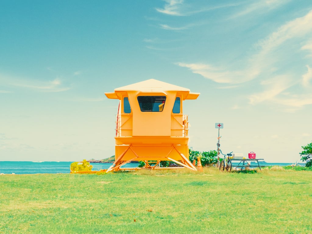 Bright yellow lifeguard tower on a grassy shore with turquoise ocean and blue sky behind