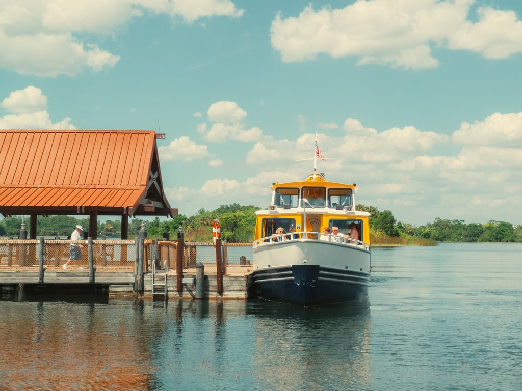 Yellow-and-white passenger boat moored at a wooden dock next to an orange-roofed pavilion with an American flag flying