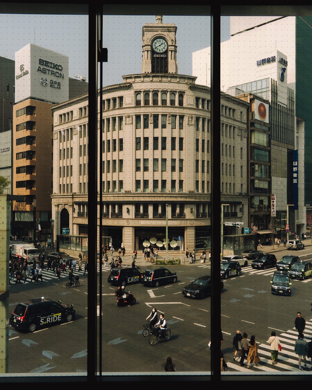 View through window panes onto a busy city intersection with a neoclassical building topped by a Seiko clock