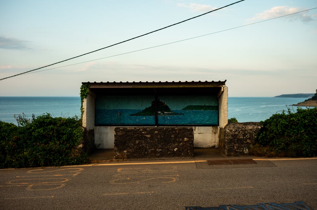 Concrete seaside shelter with a painted mural of an island and sailboats, a stone bench in front and calm sea behind