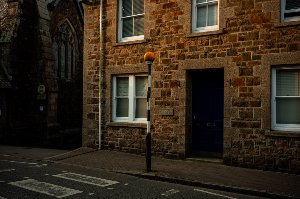 Stone building with a dark blue door and a plaque reading Old Police House, with an orange belisha beacon nearby