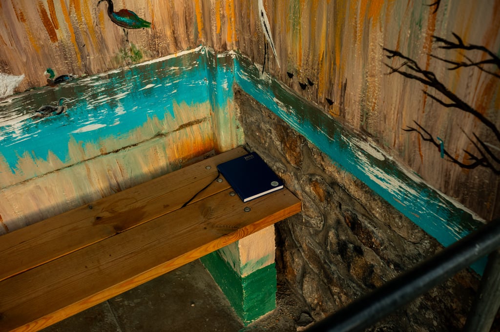 A wooden bench in a painted corner with a blue 2018 notebook, surrounded by worn turquoise and brown mural painting