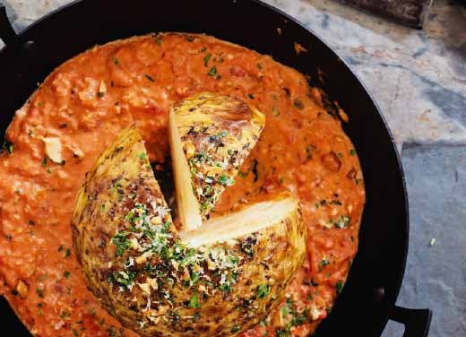 Roasted celeriac in a rich tomato and lemon sauce, served in a pan on a granite worktop.