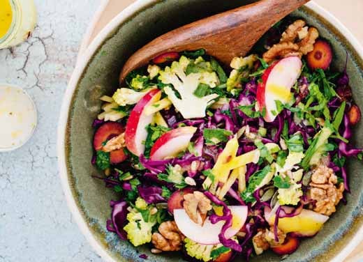 A colourful rainbow slaw in a bowl on a worktop, with a wooden spoon ready for mixing.
