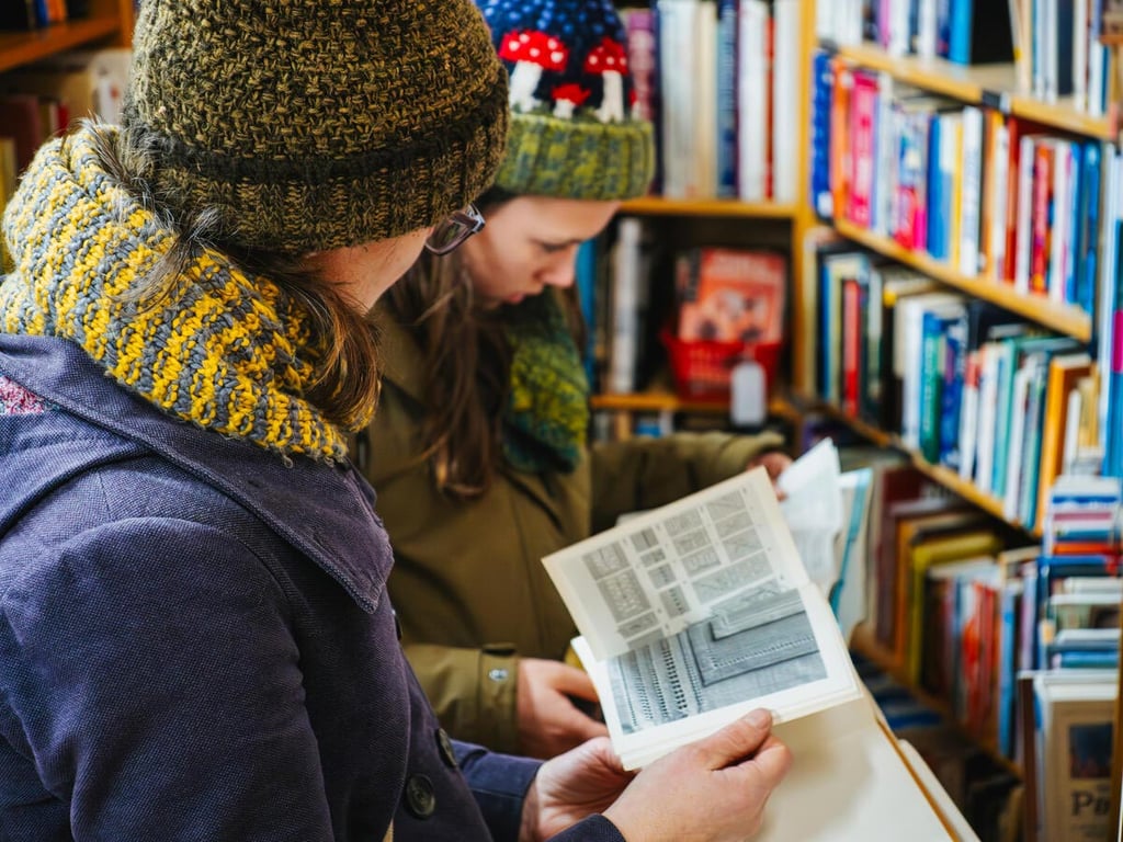 Two visitors in winter clothing reading books inside the second-hand bookshop at Blickling, Norfolk.