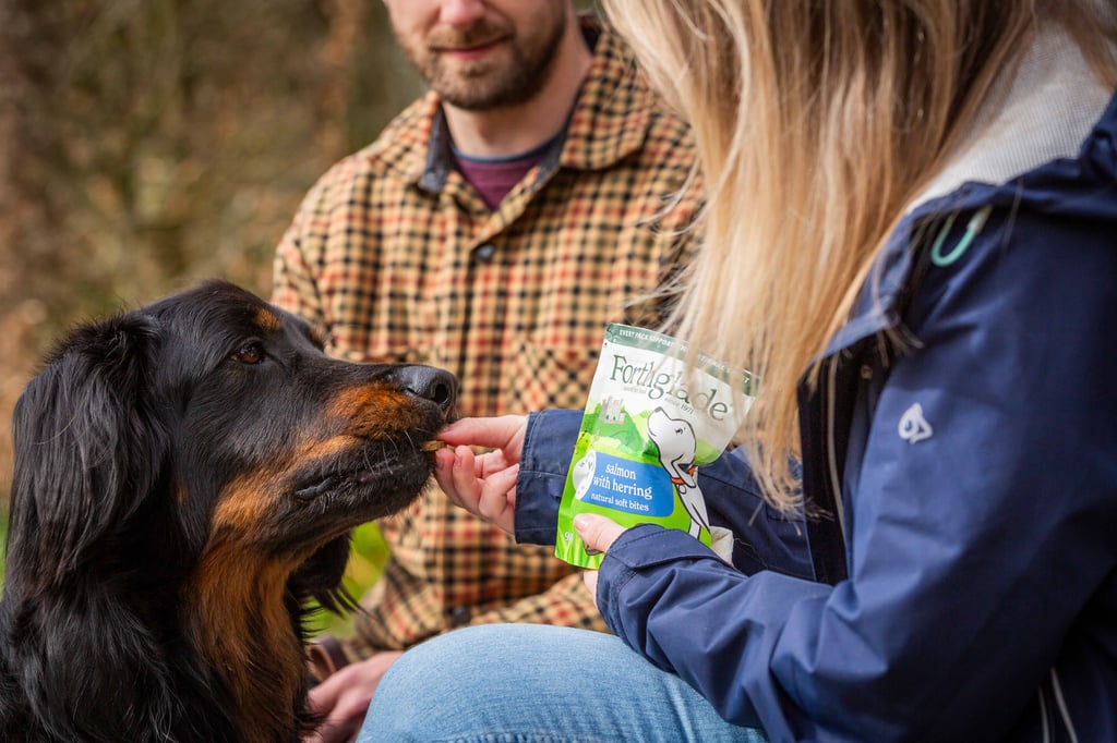 Dog receiving Forthglade treats from two people in an autumn setting.