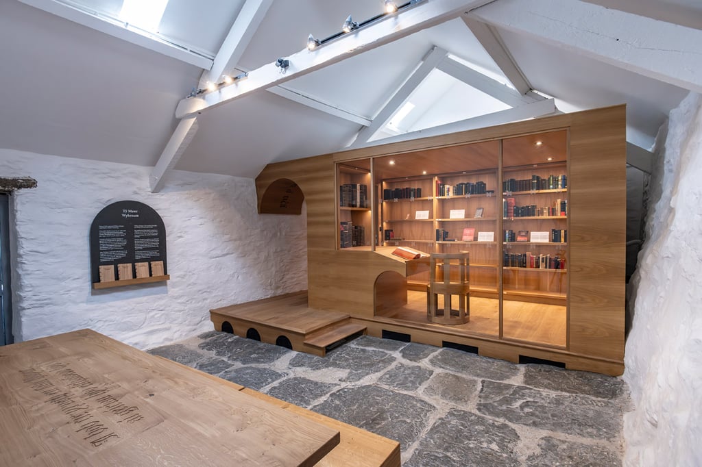 Wooden and glass walk-in library pod, Y Llyfrgell, displaying a collection of foreign language Bibles.