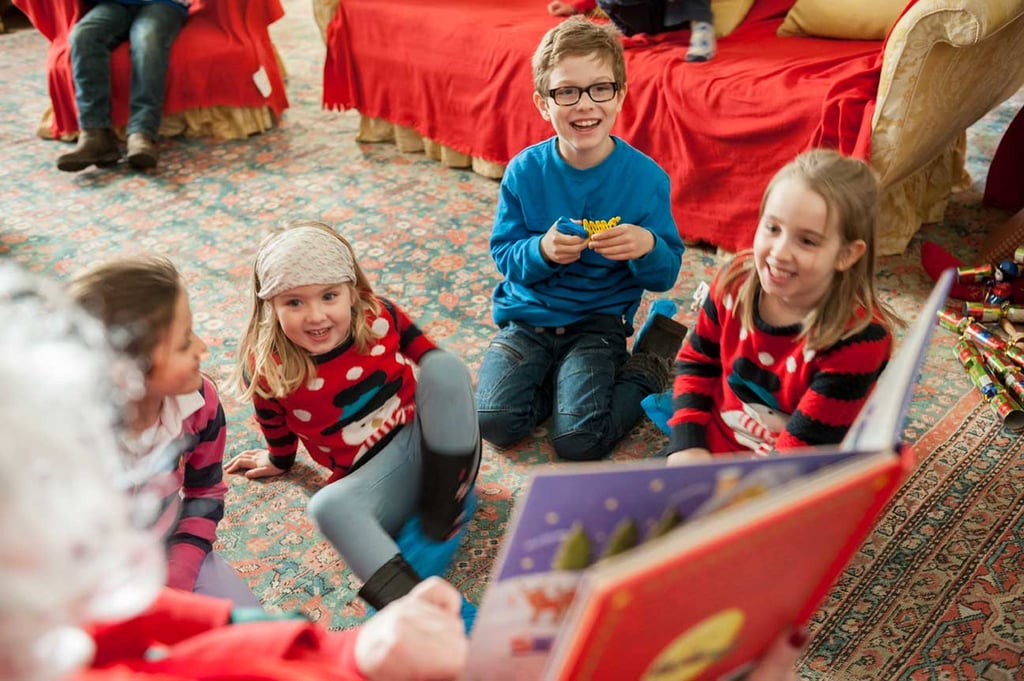 Santa Claus reading a book to a group of children inside the library at Wallington during Christmas.
